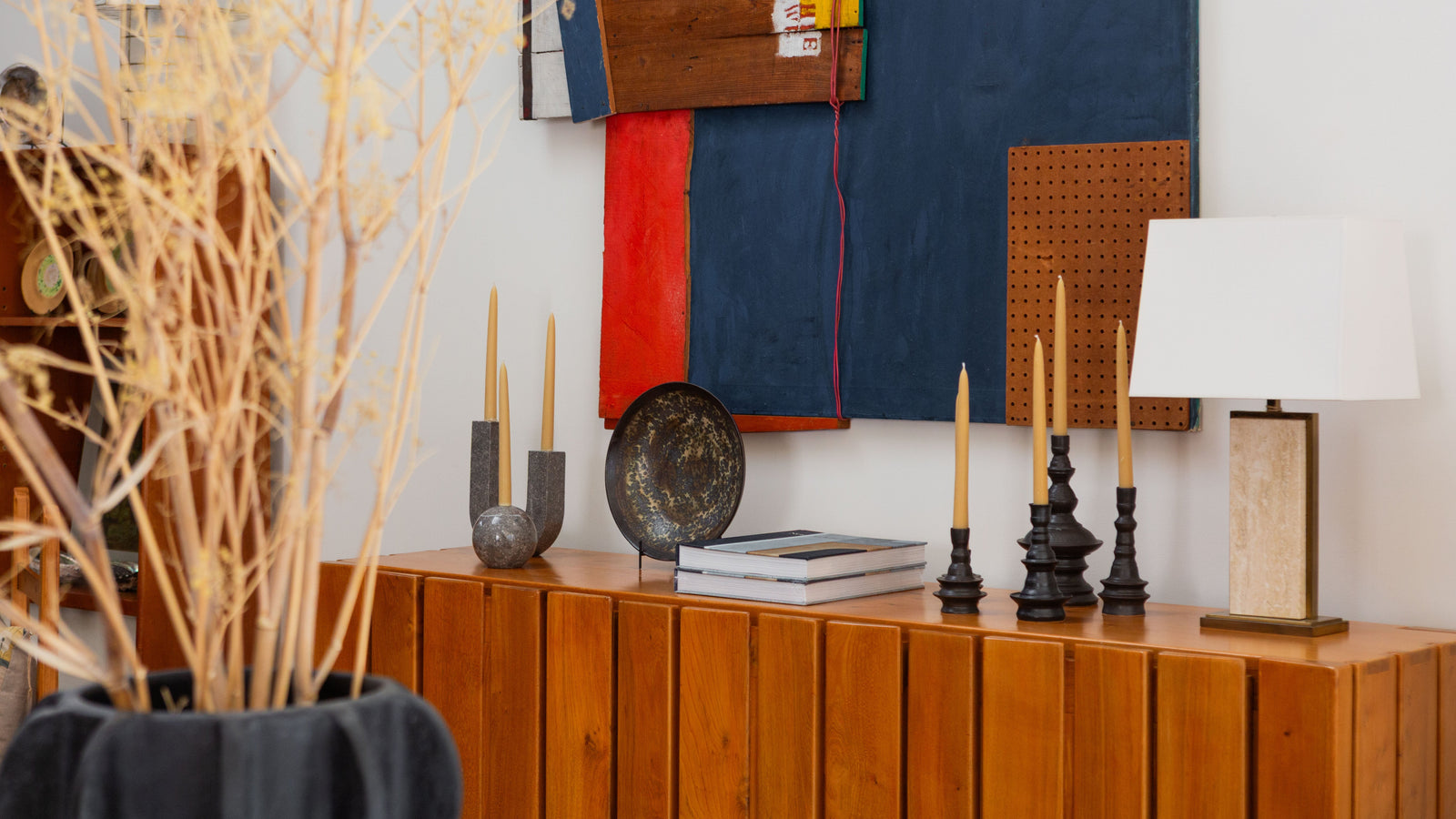Decorative setting with a wooden cabinet, candles, and a colorful abstract painting on a white wall.